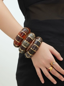 Detail of stacked leopard print resin bangles and gold gemstone rings on model's wrist