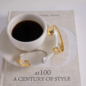 Macro view of minimalist open cuff bracelets in gold and silver with drop-shaped ends