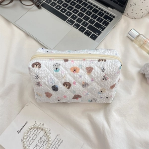Quilted white cosmetic bag with cute dog patterns shown next to a laptop and books
