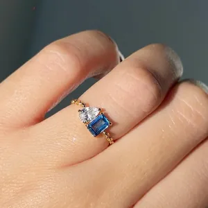 Close-up of gold chain ring with pear-cut white zircon and emerald-cut blue gemstone