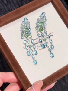 Detail of silver drop earrings with light blue and green oval zircons on display tray