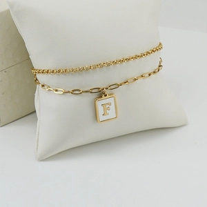 Double-layered gold stainless steel paperclip bracelet with letter F pendant on white pillow