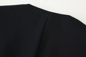 Close-up detail of black fabric texture and fine stitching on a V-neck blazer sleeve