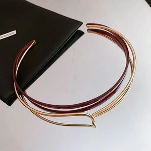 Close-up of a double-layered gold metal and resin collar necklace on a mirror surface