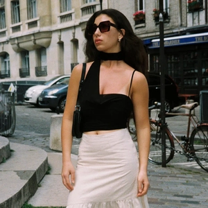 Street style view of a woman wearing a black one-shoulder tie-up crop top with a beige skirt