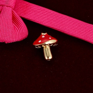 Macro view of gold mushroom charm with red enamel and white spots on velvet