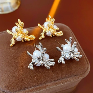 Makroansicht von gold- und silberfarbenen Blumenohrringen mit Perlen auf Samt