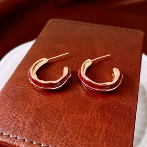 Macro view of C-shaped gold-plated hoop earrings with red enamel on leather