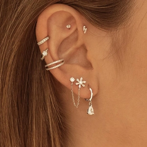 Detail of silver S925 flower earrings with cubic zirconia stones on multiple ear piercings