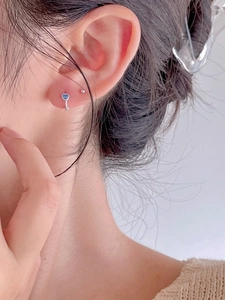 Detailed close-up of a silver heart-shaped hoop earring with a light blue zircon gemstone