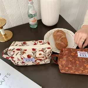 Détail de trousses de maquillage en velours côtelé à fleurs avec poignée sur table en bois