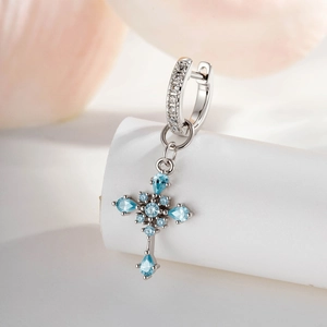 Minimalist silver cross drop hoop earring with light blue zircons on white pedestal
