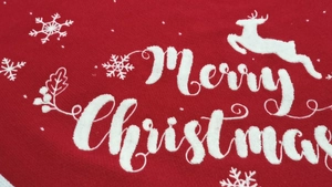 Detail of red knit Christmas tree skirt with white Merry Christmas embroidery
