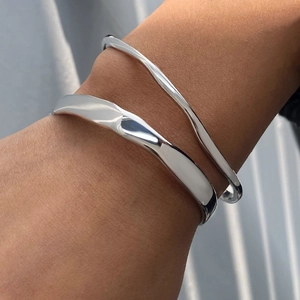 Close-up of a wide wavy silver bangle and slim streamlined cuff layered on a wrist
