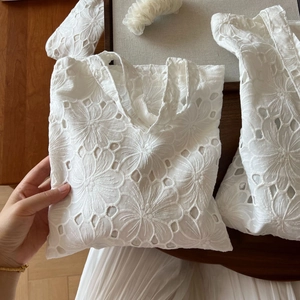 Detail of white cotton handbag featuring intricate floral embroidery and hollow-out design