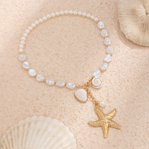 Golden starfish and shell pendant necklace with white baroque pearls on sand texture