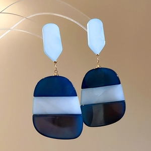 Detailed close-up of blue oval acetate pendant earrings on a modern jewelry display