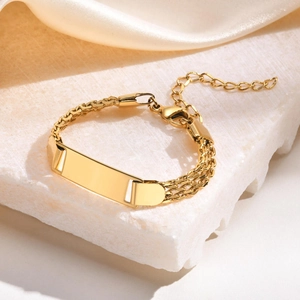Detail of a polished gold ID plaque on a double-row woven mesh chain bracelet