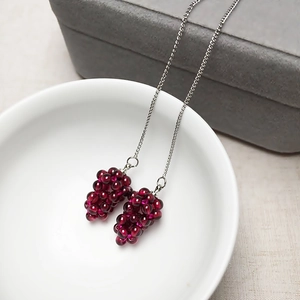 Macro shot of handmade pomegranate-red grape cluster earrings on a silver chain