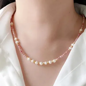 Pink natural stone and freshwater pearl necklace with gold accents on a white shirt