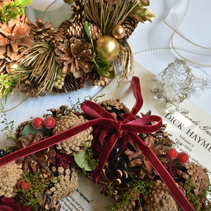 Vintage Christmas wreath featuring natural pine cones, red berries, and velvet ribbon bow
