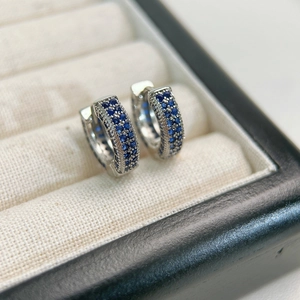 Close-up of silver hoop earrings with blue pavé stones on beige velvet jewelry box