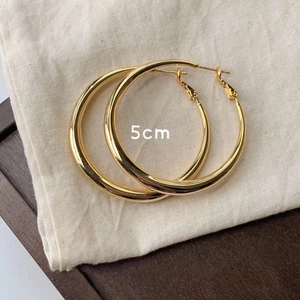 Detailed view of 5cm gold metal hoop earrings on textured fabric background