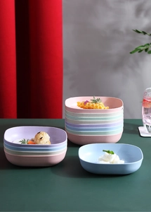 Macro detail of pastel square wheat straw plates stacked with food on a dark green table