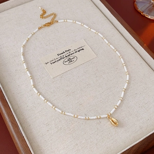 Detail of beaded necklace featuring a gold shell pendant on a soft linen jewelry box
