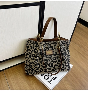 Detail of leopard print canvas tote bag featuring brown PU leather straps and metal hardware