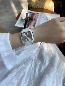 Close-up of a square silver watch with a white silicone strap on a model's wrist