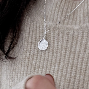 Minimalist 925 sterling silver wavy coin necklace shown on a beige knitted sweater