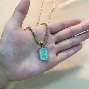 Golden twist chain necklace with iridescent blue square zircon pendant held by hand