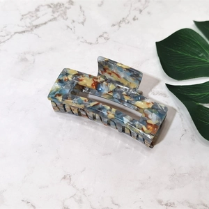 Close-up of rectangular acetate hair claw clip with colorful marble pattern on marble base