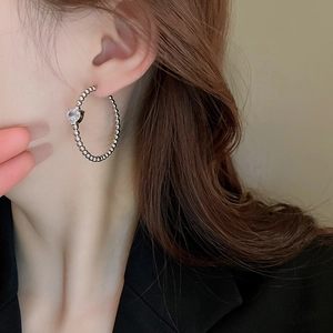 Close-up of a silver beaded hoop earring with heart-shaped crystal on female model