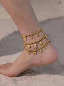 Nahaufnahme von goldenen Fußkettchen mit Herz- und Sternanhängern auf feinem Sand