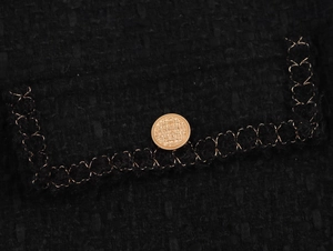 Dettaglio macro della tasca in tweed nero con ricamo a catena dorata e bottone in metallo