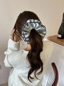 Detail of a large blue striped scrunchie with refined navy blue trim on a ponytail hair