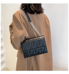 Detail of a black quilted crossbody bag with silver chain strap on a camel suit