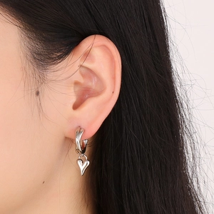 Close-up of a silver heart-shaped pendant earring worn on ear with polished finish