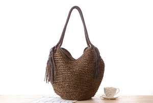 Gros plan détaillé du sac hobo en paille tressée marron avec franges sur table en bois
