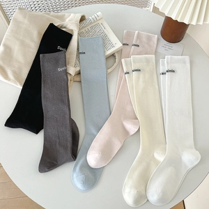Colorful long knit socks in pastel tones laid out on a white table with home decor accents