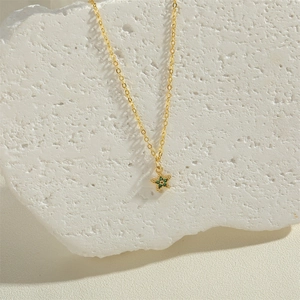 Gold star necklace with green zircon pendant displayed on a textured white rock base