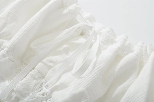 Detail shot of the white textured fabric featuring delicate lace and elegant ribbon ties