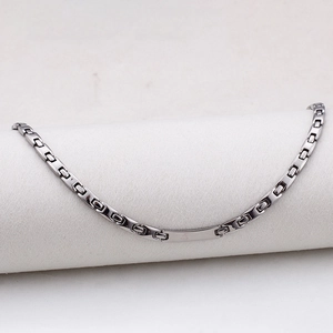 Close-up of polished silver steel bracelet with a blank rectangular ID plate on white stand