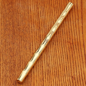 Close-up of golden bamboo shaped brass pen with Chinese calligraphy on wood background