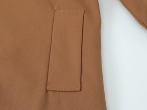 Detail of side pocket stitching on brown trench coat with durable twill fabric texture