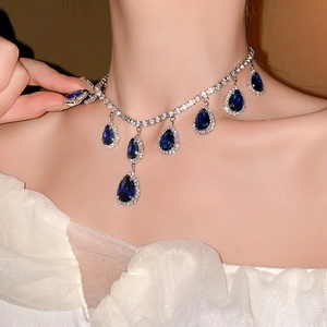 Close-up of a silver necklace featuring seven deep blue teardrop gemstones and pave crystals