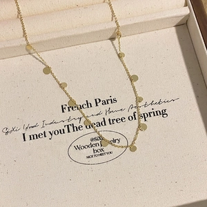 Detail of gold necklace with round sequins in a beige textured jewelry box