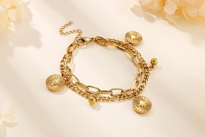 Detail of double-layer gold chain bracelet with sunburst coin charms and dried flower petals